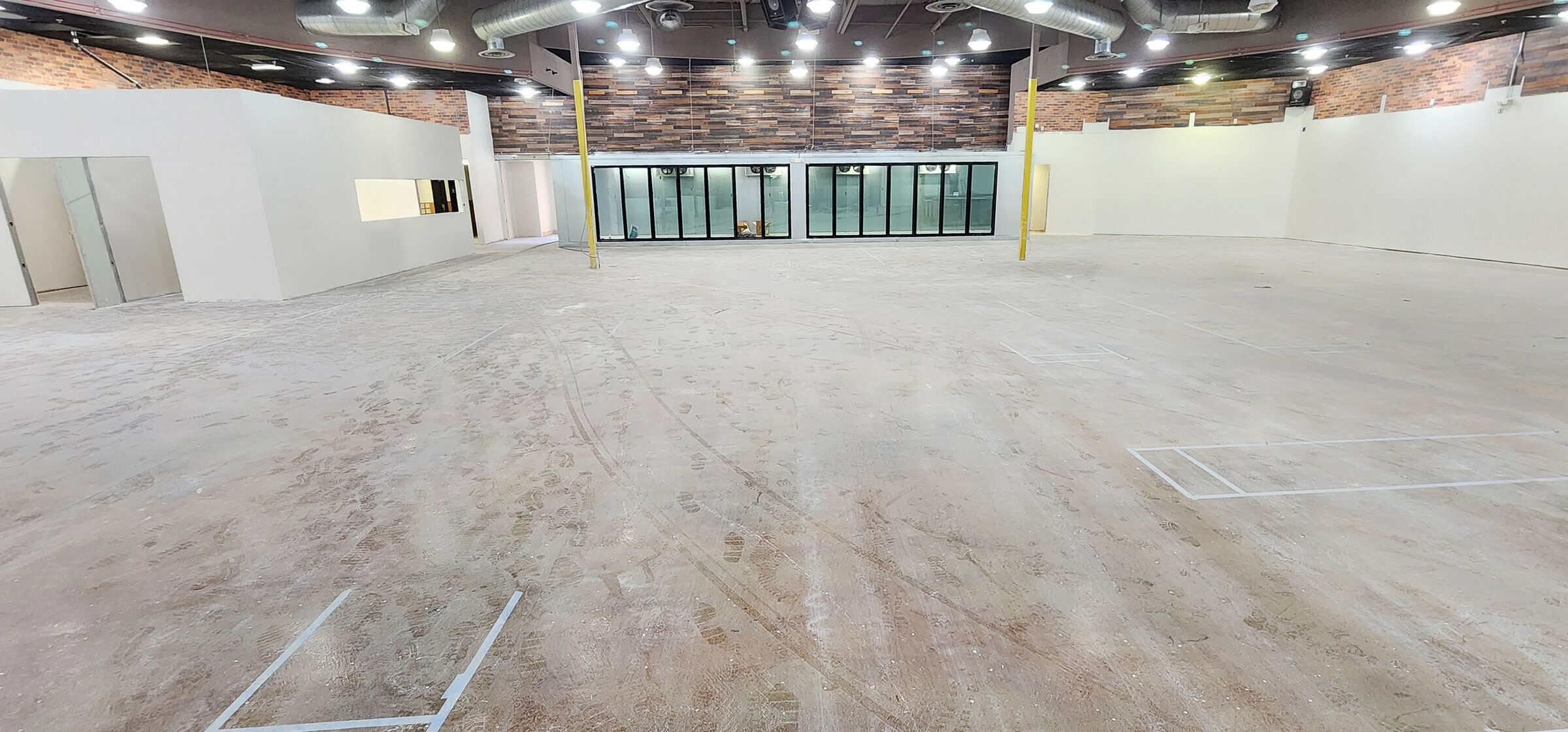 The same retail floor before polishing: raw concrete with adhesive residue, tire tracks and layout tape.
