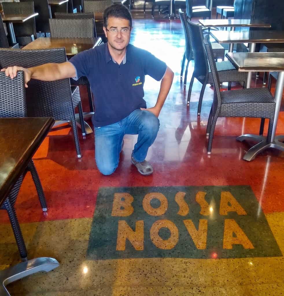 Jevan Araujo kneeling on a polished concrete floor he finished at the Bossa Nova restaurant, the logo inlaid into the slab.